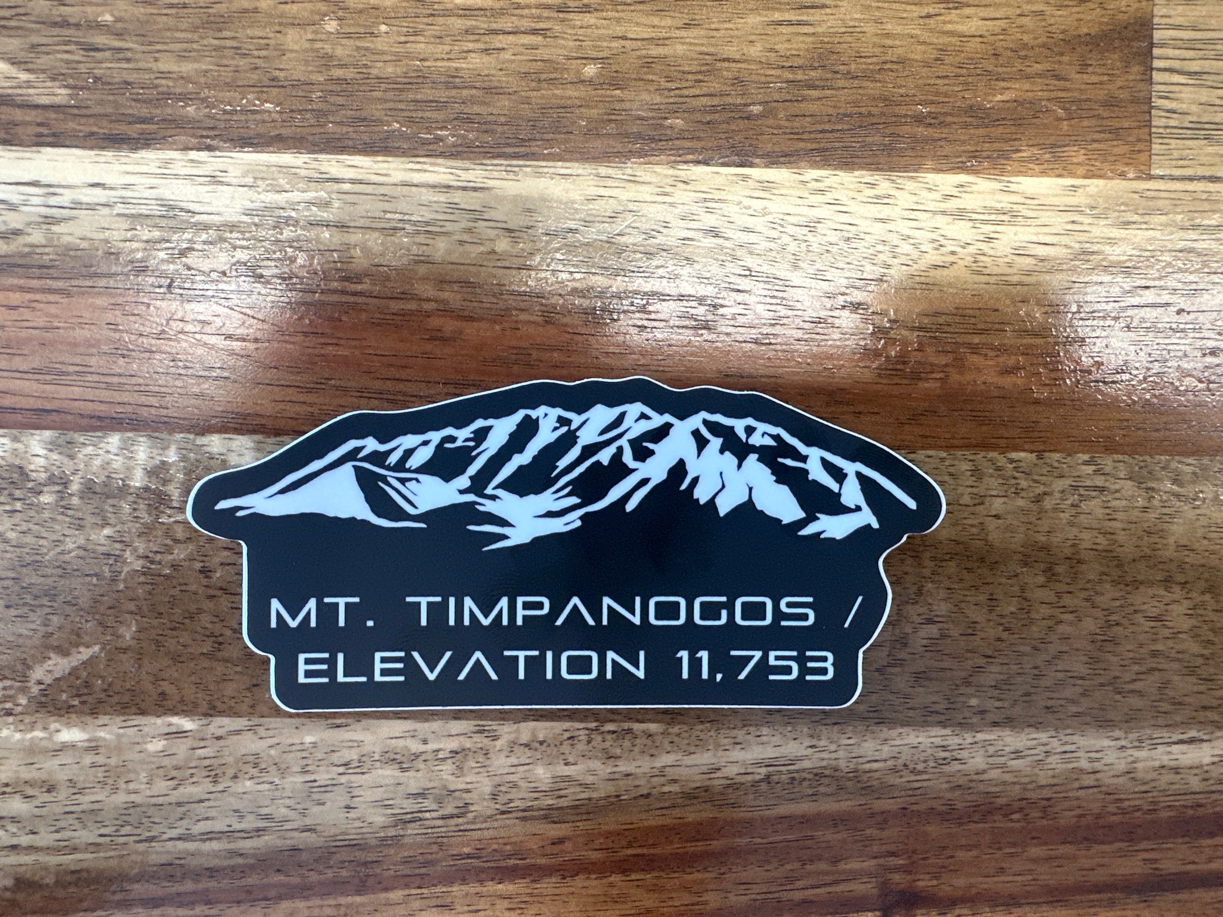 Sticker with mountain design and text on a wooden surface