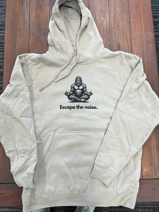 Heather Cream hoodie featuring a meditating Sasquatch graphic with the "Escape the noise" slogan, ideal for those who love nature and outdoor relaxation