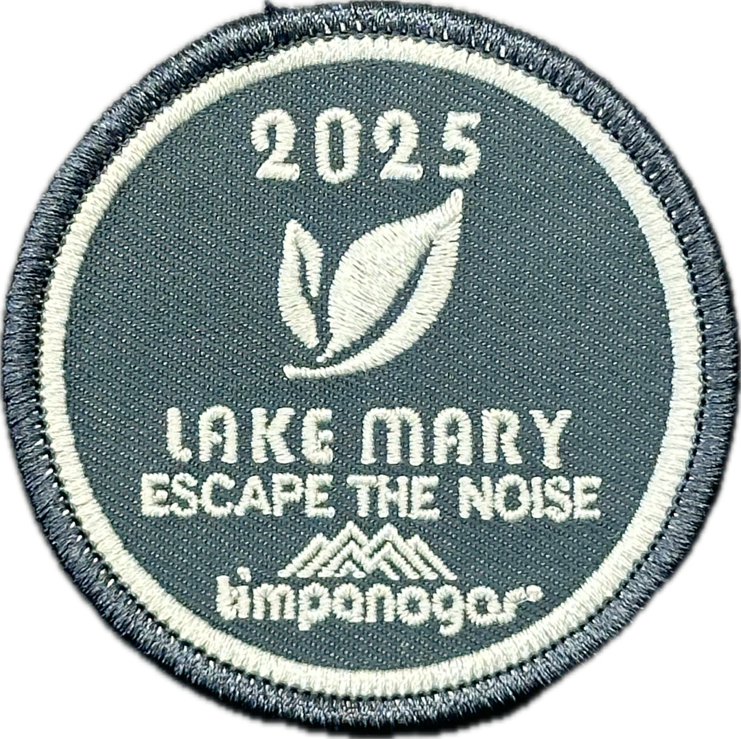 2025 Timpanogos "Lake Mary" patch in slate blue with white embroidery. Features a double leaf graphic, the phrase "Escape the Noise," and the Timpanogos Hiking Co. logo beneath.