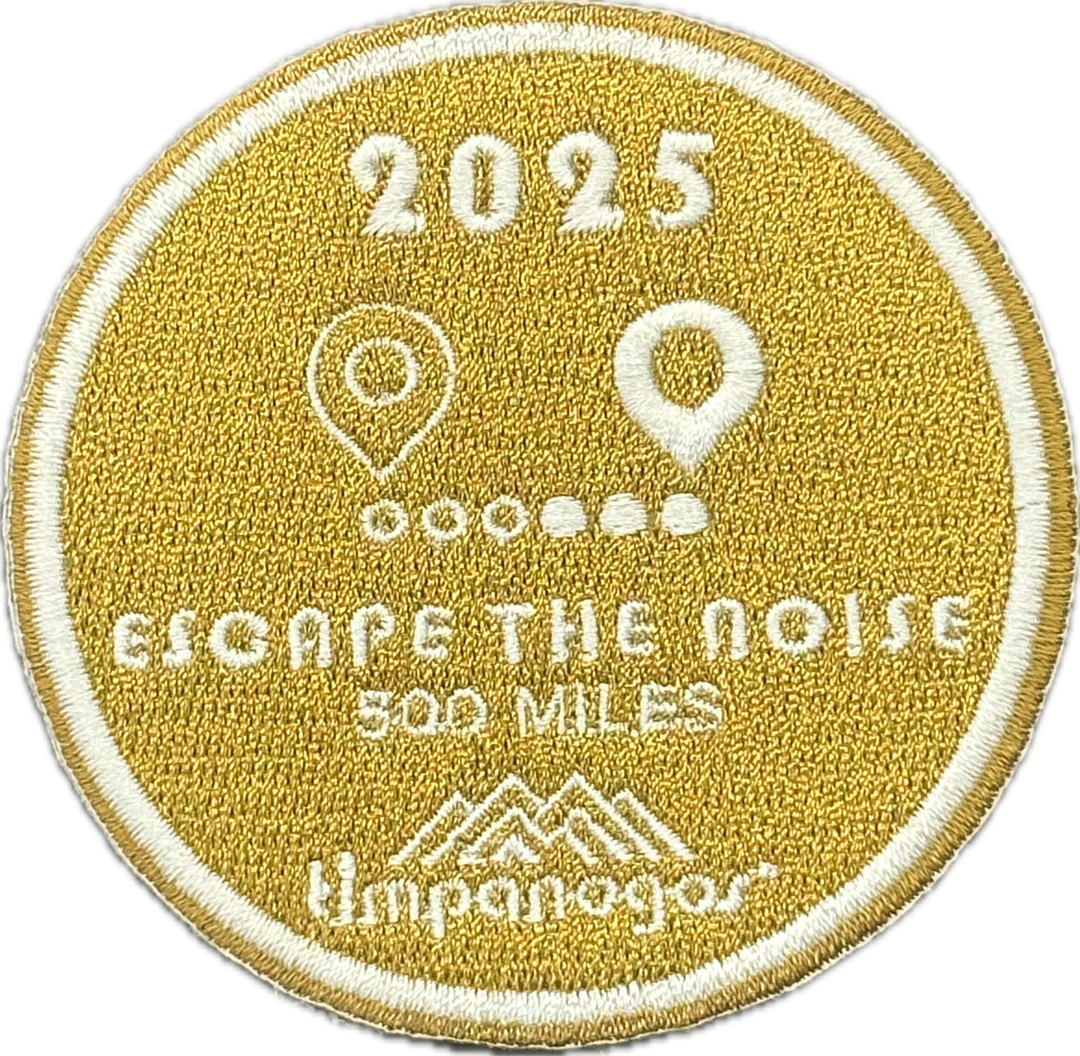 2025 Timpanogos "Escape the Noise" patch in gold with white stitching, earned for completing 500 miles. Features location pin icons connected by a dotted path above the bold phrase and the Timpanogos Hiking Co. logo.