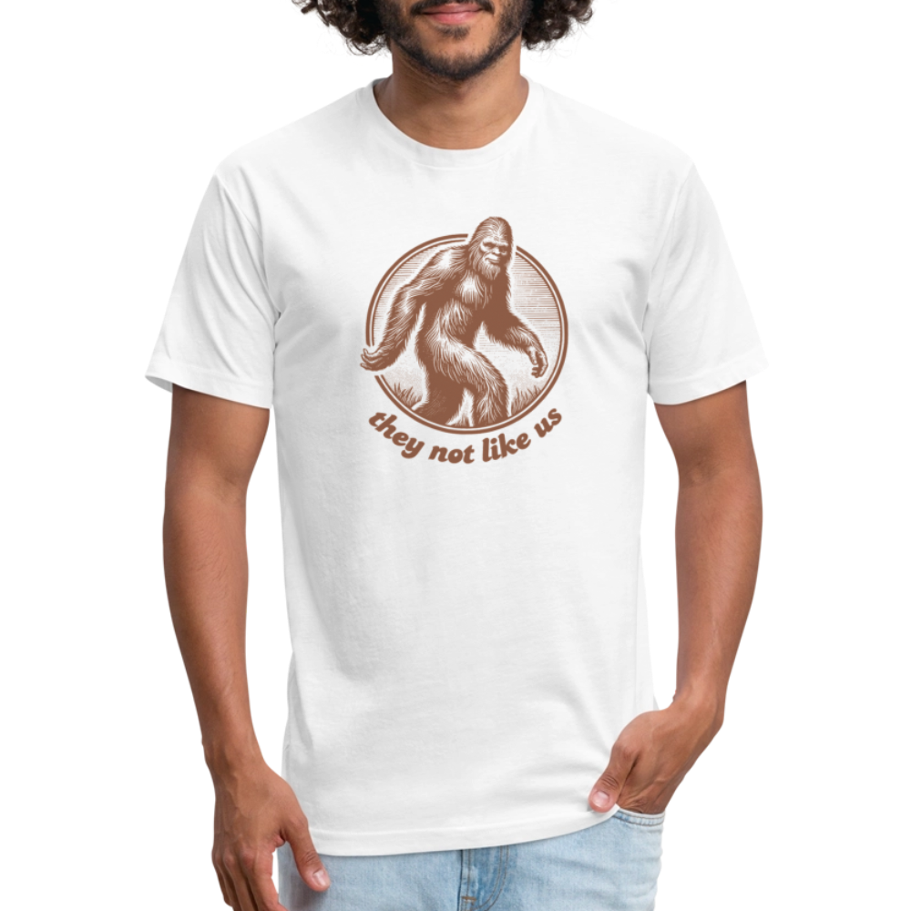 White unisex t-shirt featuring a vintage-style brown illustration of Bigfoot inside a circular frame with the phrase "they not like us" curved below. The design evokes mystery and outdoor adventure with a minimalist, rustic look.