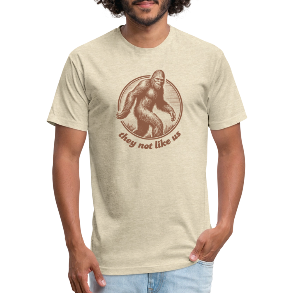 heather cream unisex t-shirt featuring a vintage-style brown illustration of Bigfoot inside a circular frame with the phrase "they not like us" curved below. The design evokes mystery and outdoor adventure with a minimalist, rustic look.