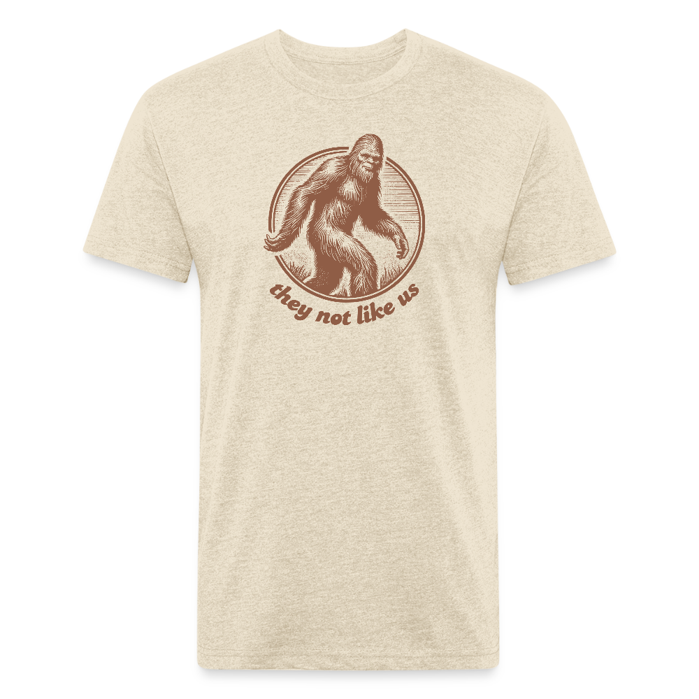 heather cream unisex t-shirt featuring a vintage-style brown illustration of Bigfoot inside a circular frame with the phrase "they not like us" curved below. The design evokes mystery and outdoor adventure with a minimalist, rustic look.
