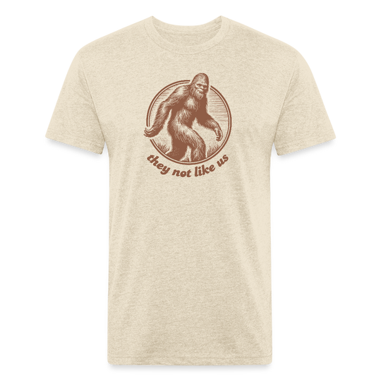 heather cream unisex t-shirt featuring a vintage-style brown illustration of Bigfoot inside a circular frame with the phrase "they not like us" curved below. The design evokes mystery and outdoor adventure with a minimalist, rustic look.