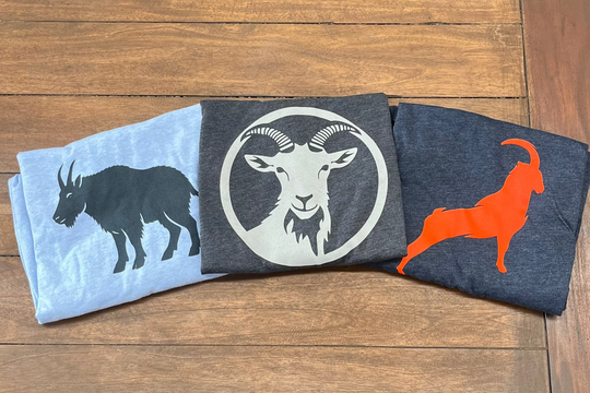 Three folded shirts with goat designs on a wooden surface